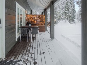 A wooden deck with a table and chairs, a snow-covered landscape, and a wooden fence with string lights. - Villa sukka a by Interhome (Kuusamo)