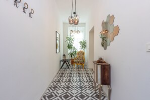 A hallway with patterned flooring, a wooden console table, a chair, and a hanging light fixture.