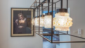 Uma escadaria com corrimão de design moderno, uma obra de arte emoldurada na parede e uma mesa com tampo de vidro e papéis.