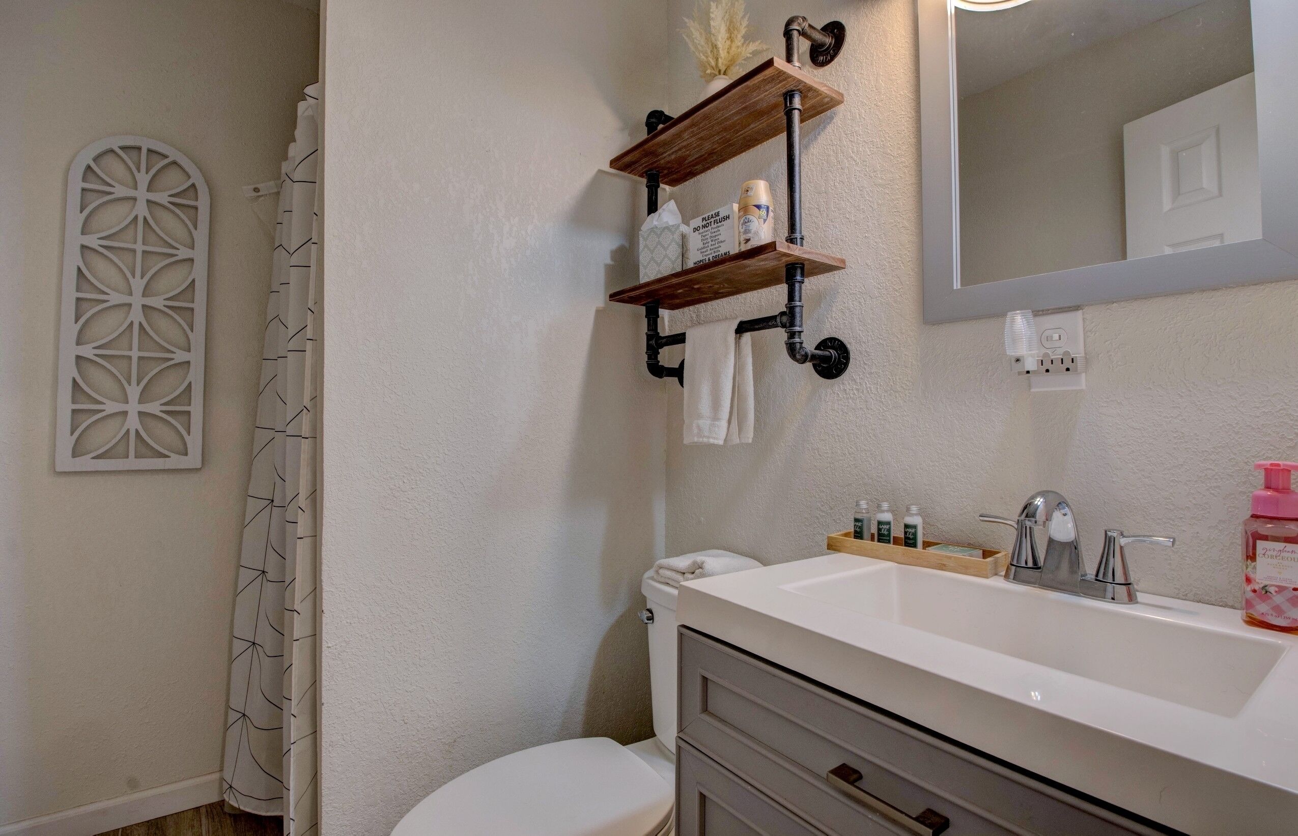 A bathroom with a white sink, a mirror, and a shower curtain. There are towels hanging on a rack and a toilet visible.
