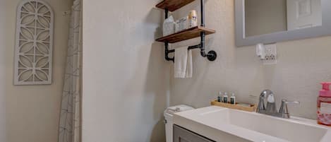 A bathroom with a white sink, a mirror, and a shower curtain. There are towels hanging on a rack and a toilet visible.