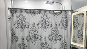 Een badkamer met een douchegordijn met een versierd zwart-wit patroon, een witte wastafel met een spiegel erboven en een toilet.
