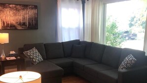 Een woonkamer met een modulaire bank, een ronde salontafel, een lamp en een schilderij aan de muur.