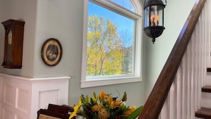 A staircase with a wooden handrail, a black lantern, a framed photograph, and a window with a view of trees.