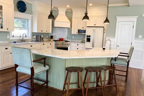 Una cocina amplia con una isla grande, taburetes de madera y lámparas colgantes.