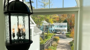 A view through a window of a residential street with houses, a pathway, and a hanging lantern.