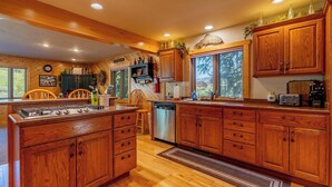 A spacious kitchen with wooden cabinets, a built-in stove, and a dishwasher. - Clarks Fork Crossing- Direct River Access, Large family Cabin! (Cody)