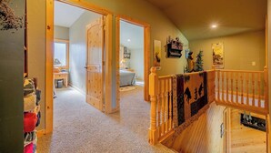 A hallway with a wooden staircase, carpeted floors, and a bed in the background. - Clarks Fork Crossing- Direct River Access, Large family Cabin! (Cody)