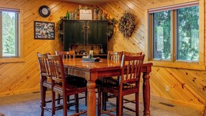 A wooden-paneled dining room with a table, chairs, a clock, and a sign that reads 'Friends Gather Here.' - Clarks Fork Crossing- Direct River Access, Large family Cabin! (Cody)