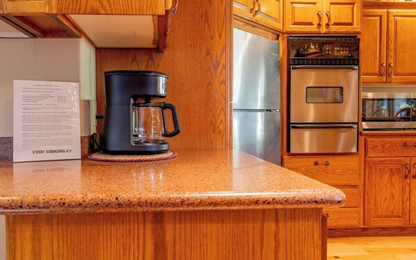 Eine Küche mit Holzschränken, einem Edelstahlkühlschrank, einem Backofen und einer Kaffeemaschine auf der Arbeitsplatte.