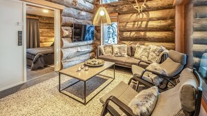 L’intérieur d’une cabane en rondins, avec un canapé, des fauteuils, une table basse et une cheminée.