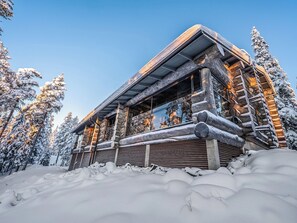 A log cabin with a covered porch, surrounded by snow-covered trees.