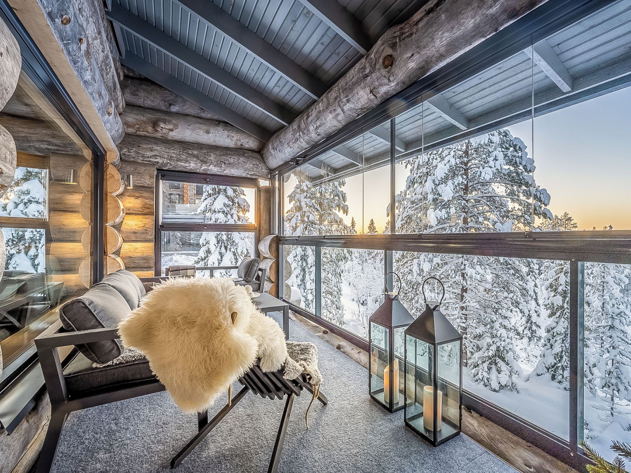 Un interior acogedor con techo de madera, un sofá, un objeto blanco mullido y vistas a árboles cubiertos de nieve.