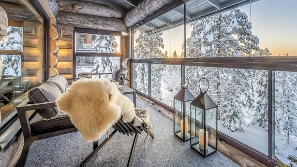 L’intérieur chaleureux d’un chalet en bois, avec une grande fenêtre donnant sur un paysage montagneux enneigé.