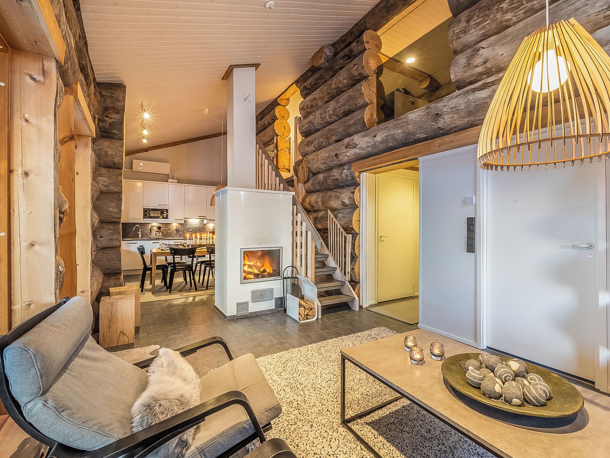 A cozy log cabin interior with a fireplace, a dining area, and a staircase leading to a loft.