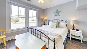 A bedroom with a bed, a nightstand, a desk, a chair, a ceiling fan, and a large window.