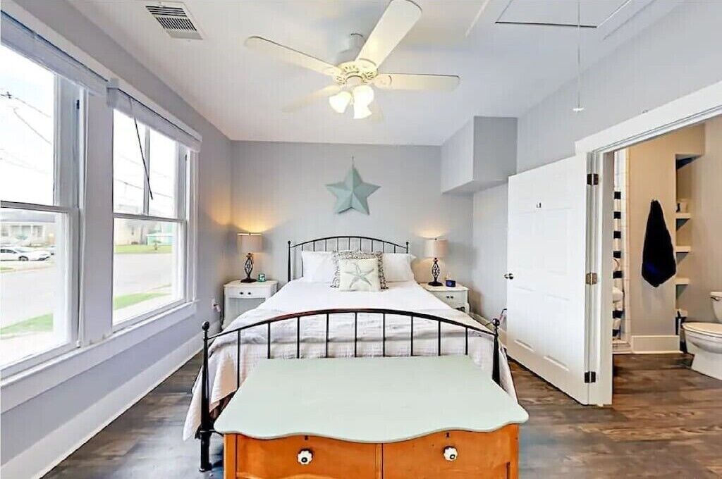 Een slaapkamer met een bed, een plafondventilator, bedlampen, een sterren decoratie aan de muur en uitzicht naar buiten door grote ramen.