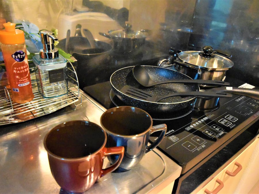 Uma cozinha com fogão, panelas, frigideiras e duas canecas no balcão.