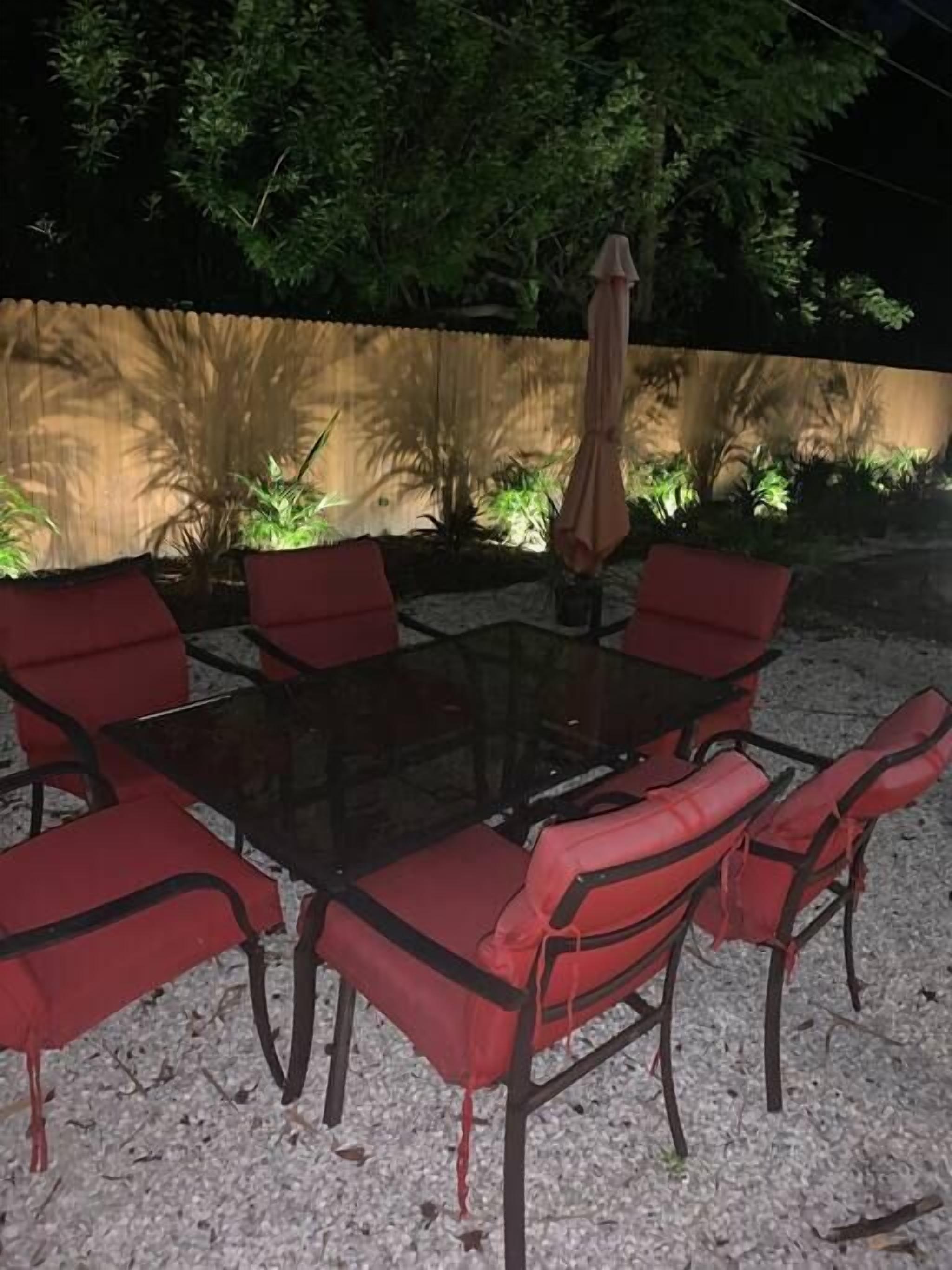 An outdoor dining area with a glass table surrounded by red cushioned chairs.