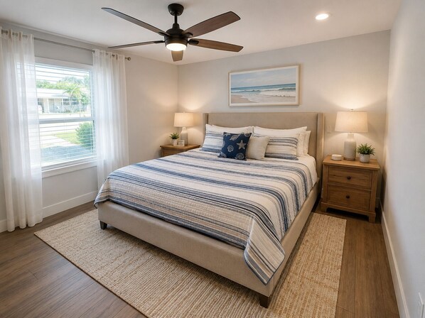 A bedroom with a bed, a ceiling fan, a window with curtains, a bedside table with a lamp, and a framed picture on the wall.