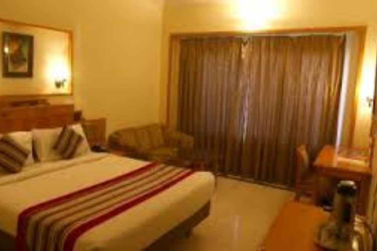 Une chambre d’hôtel avec un lit, une chaise, un bureau et un rideau.