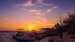 A marina with boats docked, a pier with a restaurant, and a sunset in the background. - Cute beach apartment (Savaneta)