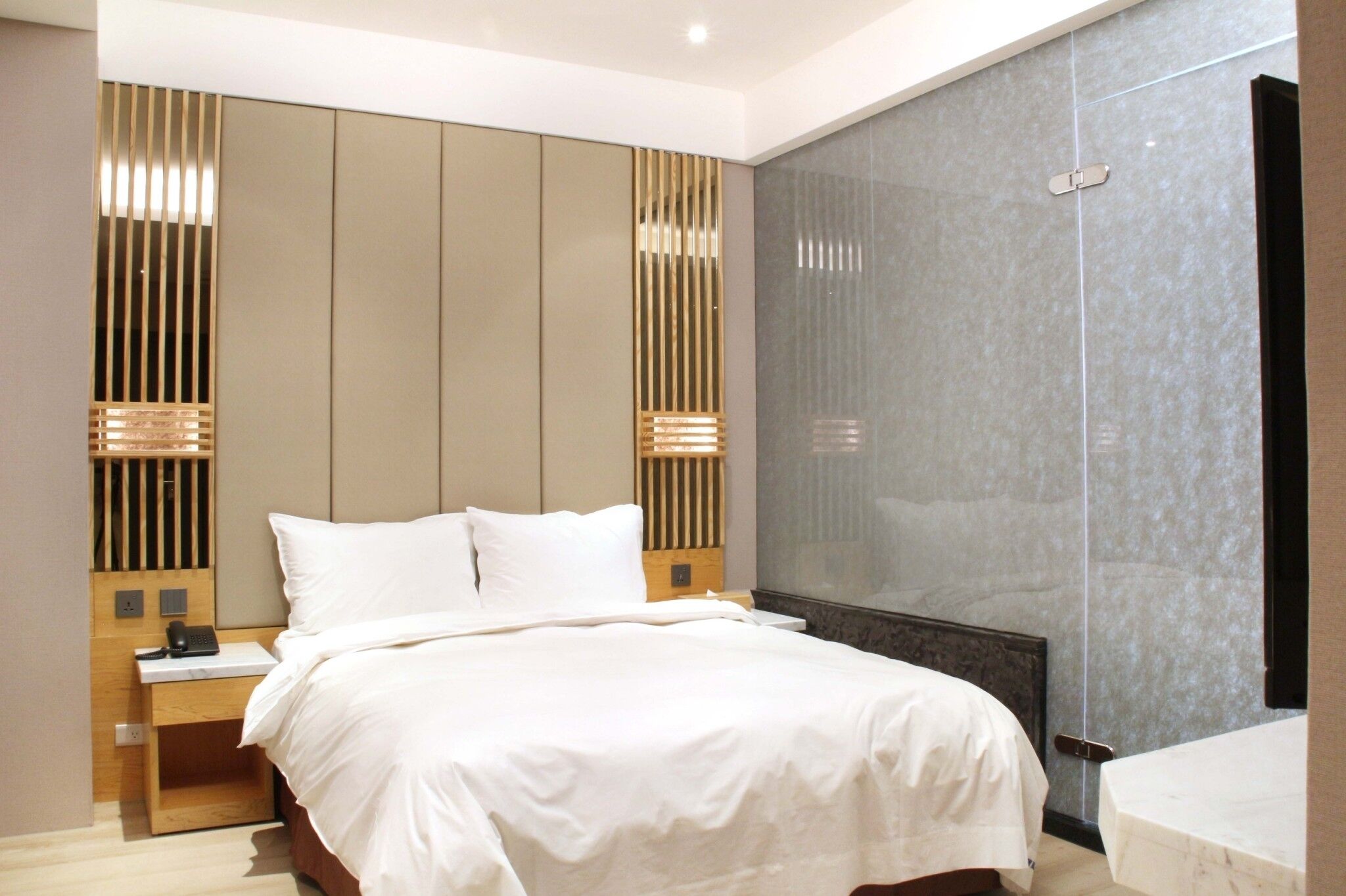 A modern hotel room with a large bed, a bedside table with a phone, and a wall-mounted radiator.