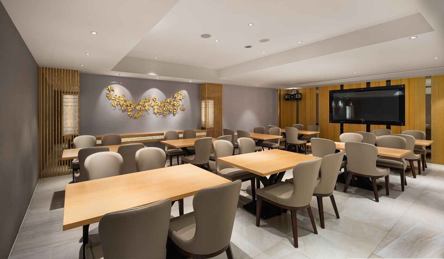 A conference room with multiple tables and chairs, a large screen, and a decorative wall piece.