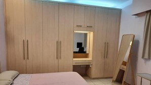 Un dormitorio con una cama, un armario, un espejo y una mesita.