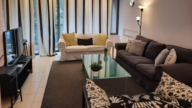 Una sala de estar moderna con una televisión, dos sofás, una mesa de centro y un gran ventanal con cortinas.
