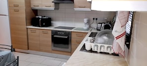 A compact kitchen with wooden cabinets, a built-in oven, a sink, and a dish drying rack.
