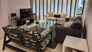 Una sala de estar moderna con una mesa de centro de vidrio, un sofá, una silla y un televisor.