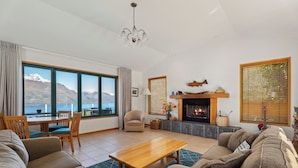 A spacious living room with a large window offering a mountain view, a fireplace, and a cozy seating area. - Deja Vu - Queenstown Holiday Home (Queenstown)