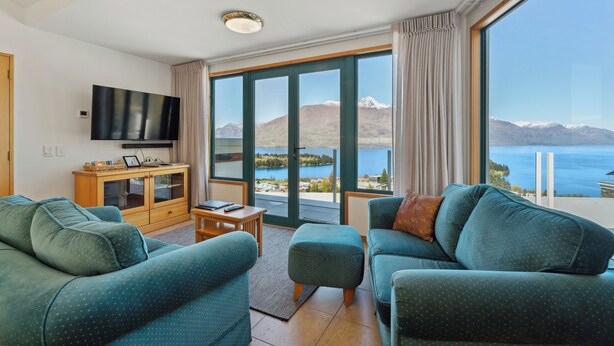 A modern living room with a large window offering a scenic view of mountains and a lake. - Deja Vu - Queenstown Holiday Home (Queenstown)