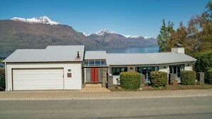 A two-story house with a garage, a front door with a red door, and a view of mountains and a lake in the background. - Deja Vu - Queenstown Holiday Home (Queenstown)