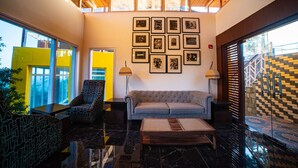 A lobby with a high ceiling, a grey sofa, patterned chairs, a coffee table, and framed pictures on the wall. - juSTa Mukteshwar Retreat & Spa (Dhari)