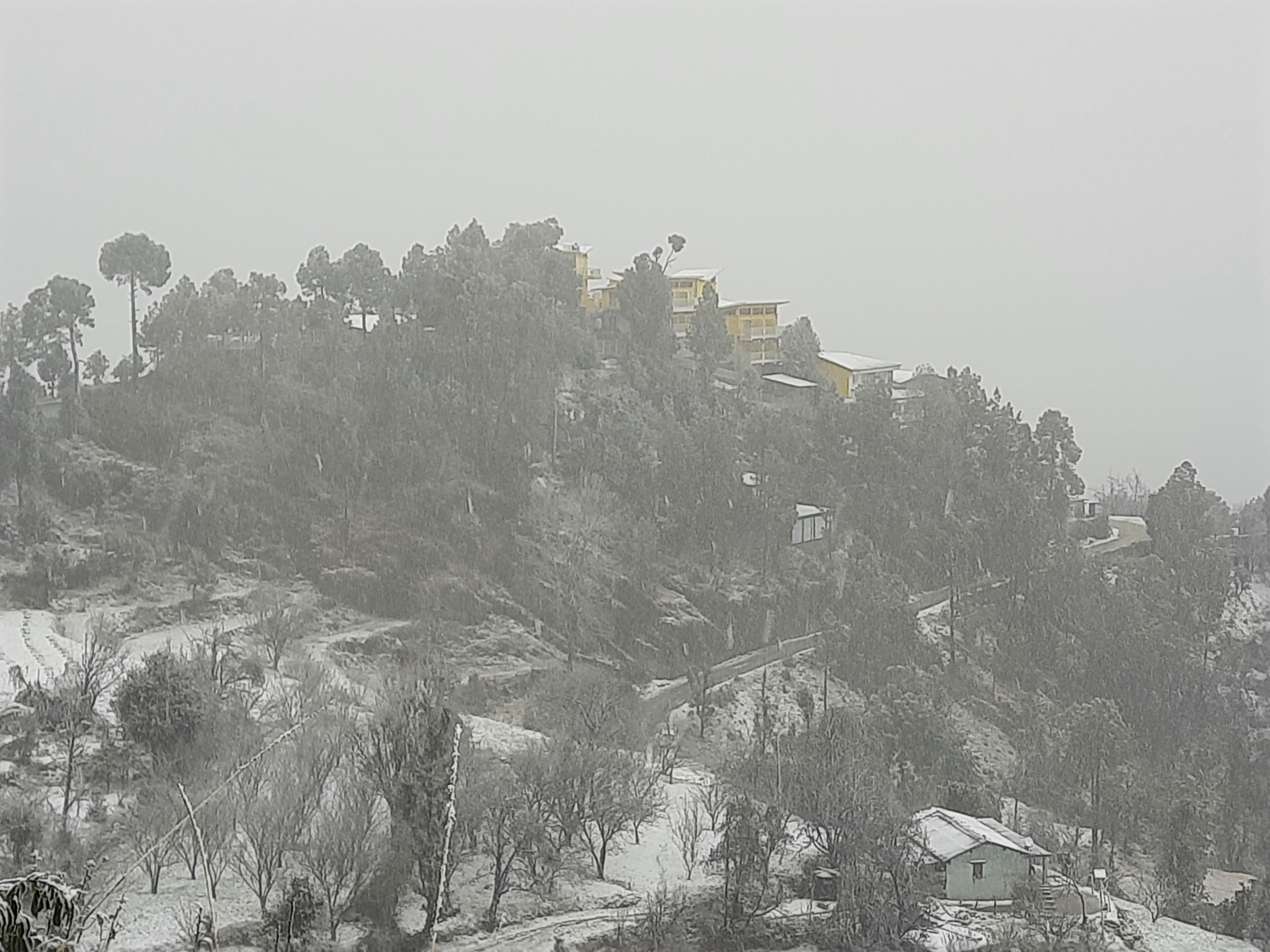 A snow-covered landscape with a small house and several buildings on a hill.