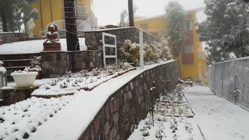 A snow-covered outdoor area with a stone wall, a statue, and a yellow building in the background.