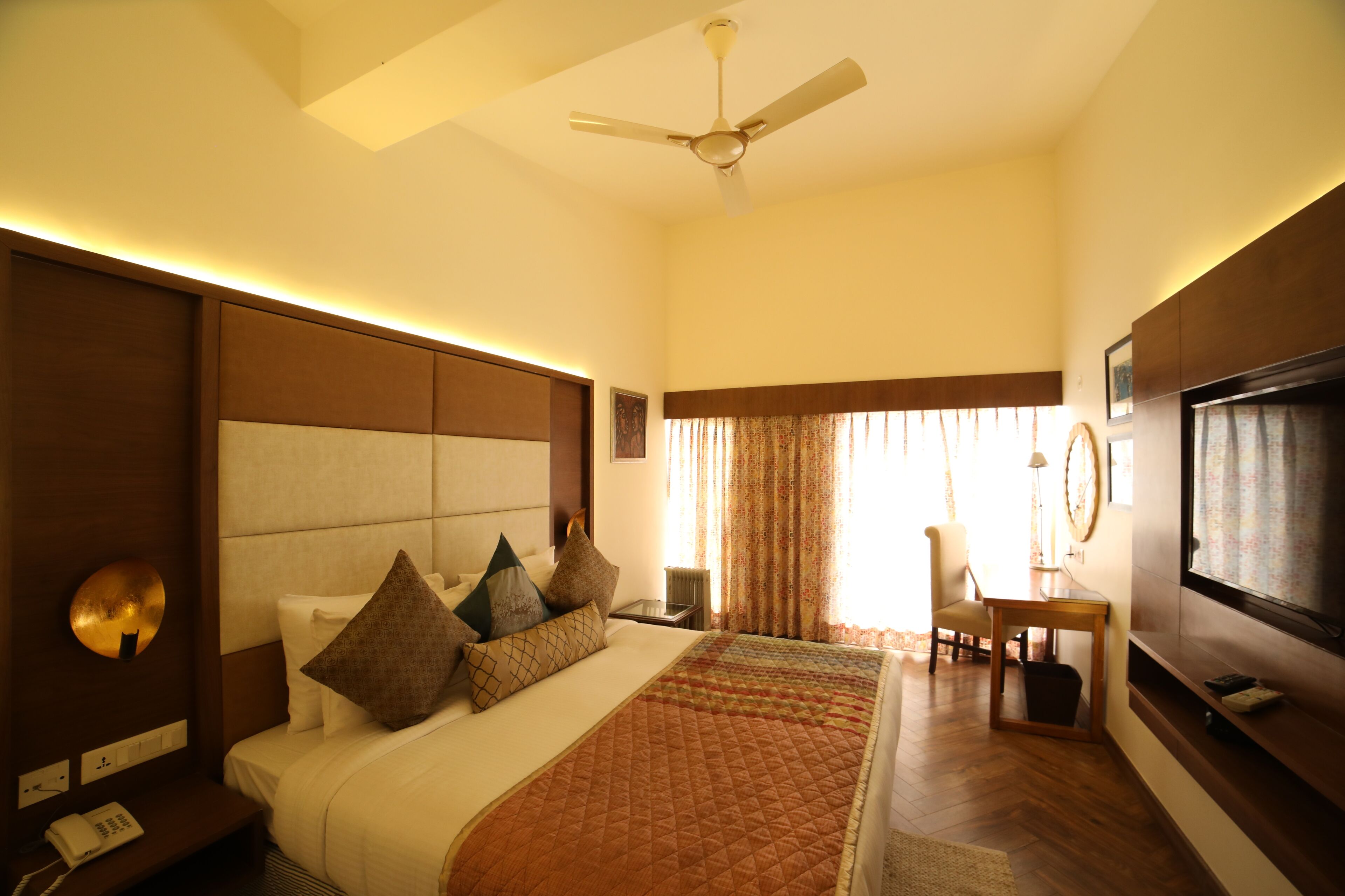 Quarto de hotel com cama grande, ventoinha no teto, televisão e secretária com cadeira.