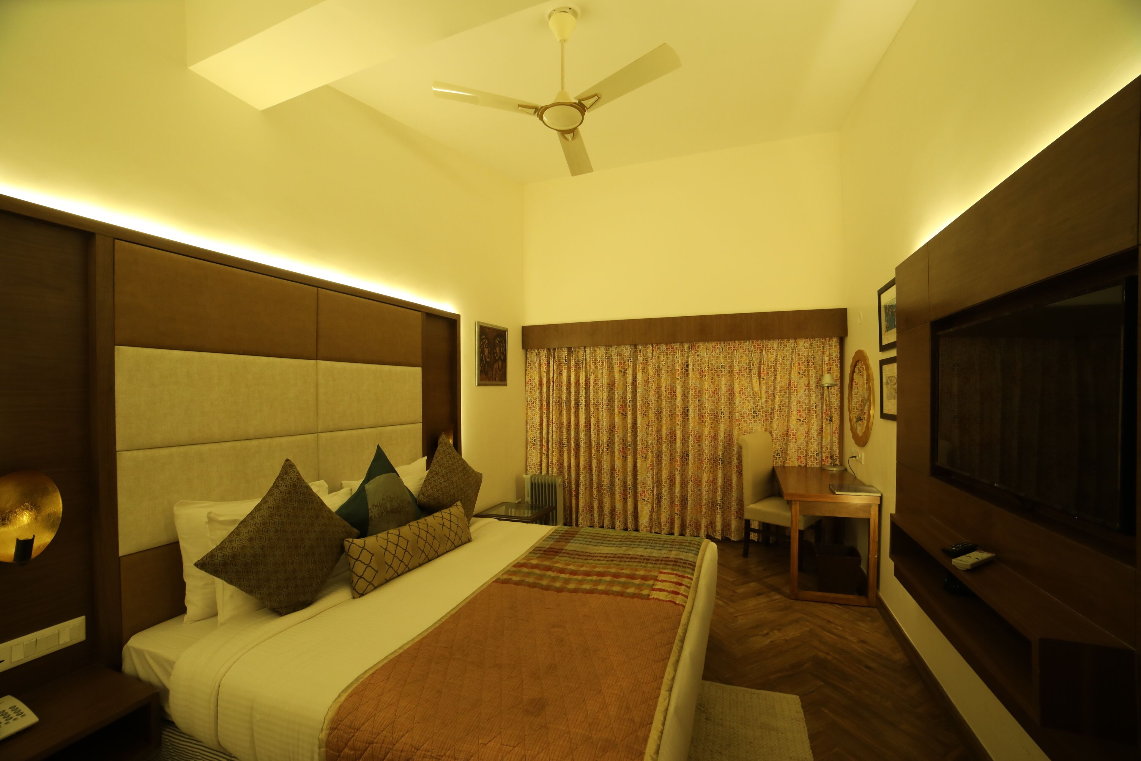 A hotel room with a large bed, a ceiling fan, a TV, and a small table.