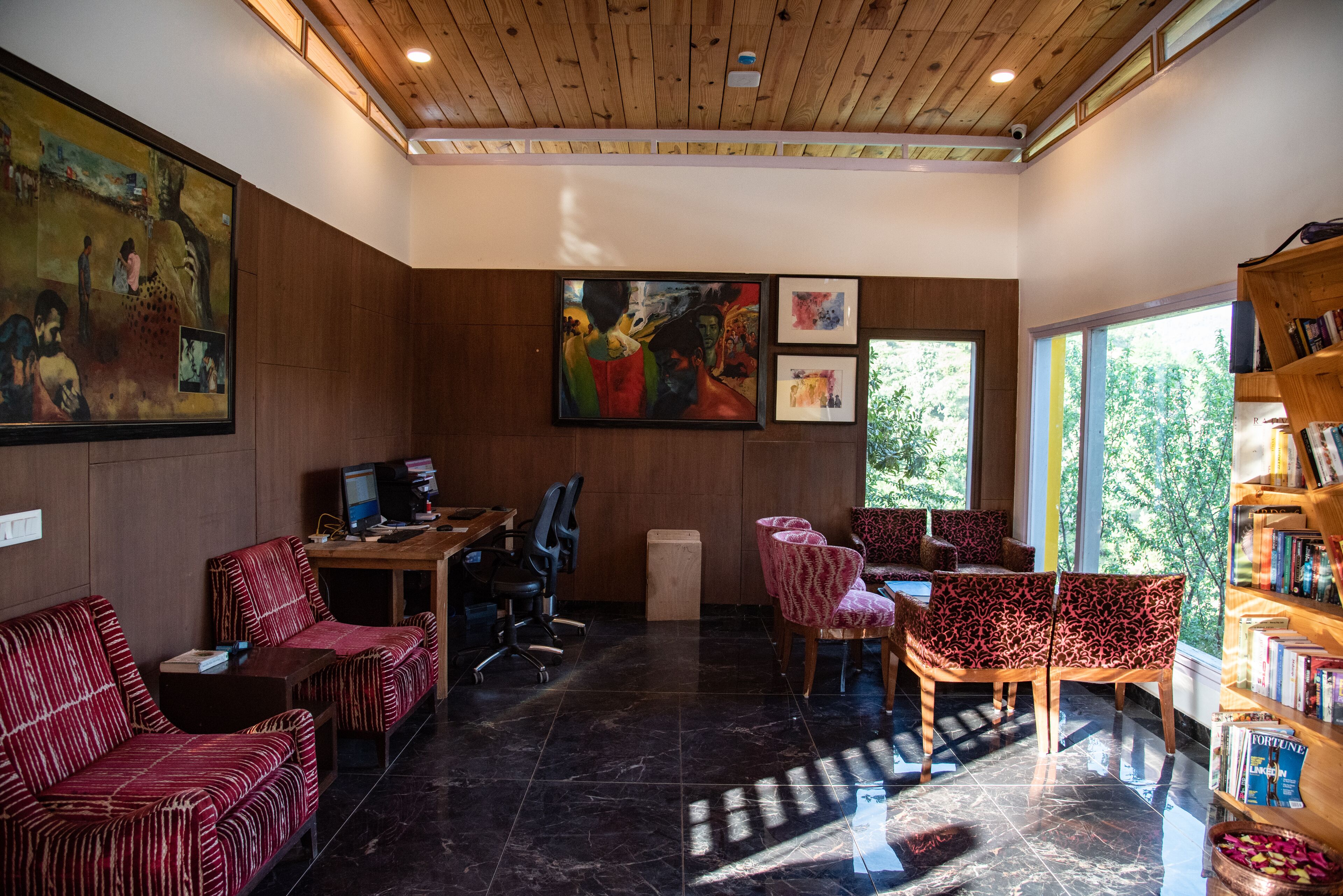 A modern interior with a wooden ceiling, a large abstract painting, a desk with a computer, and a bookshelf.