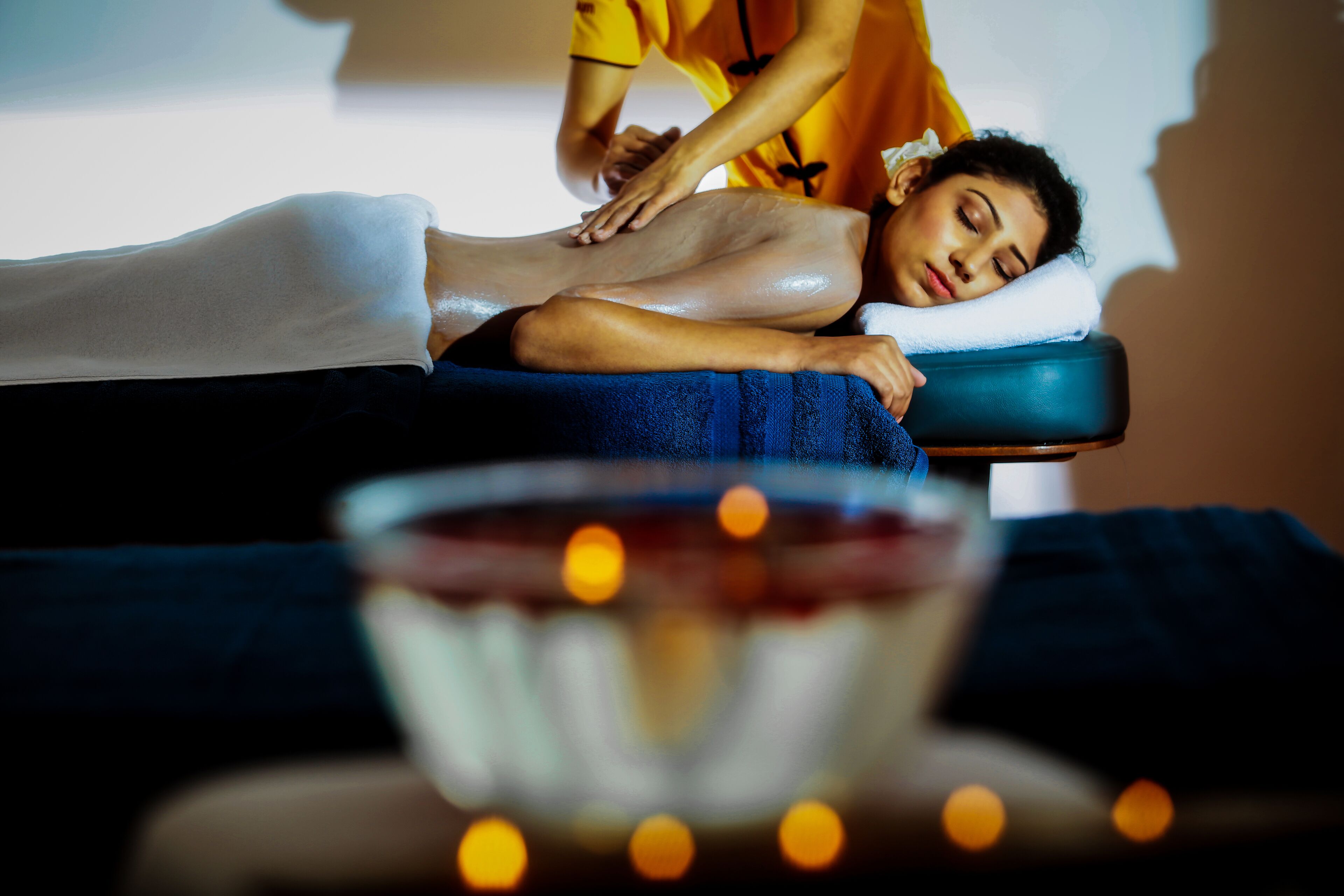 A massage therapy session in a spa setting with a massage table, a towel, and a bowl of candles.