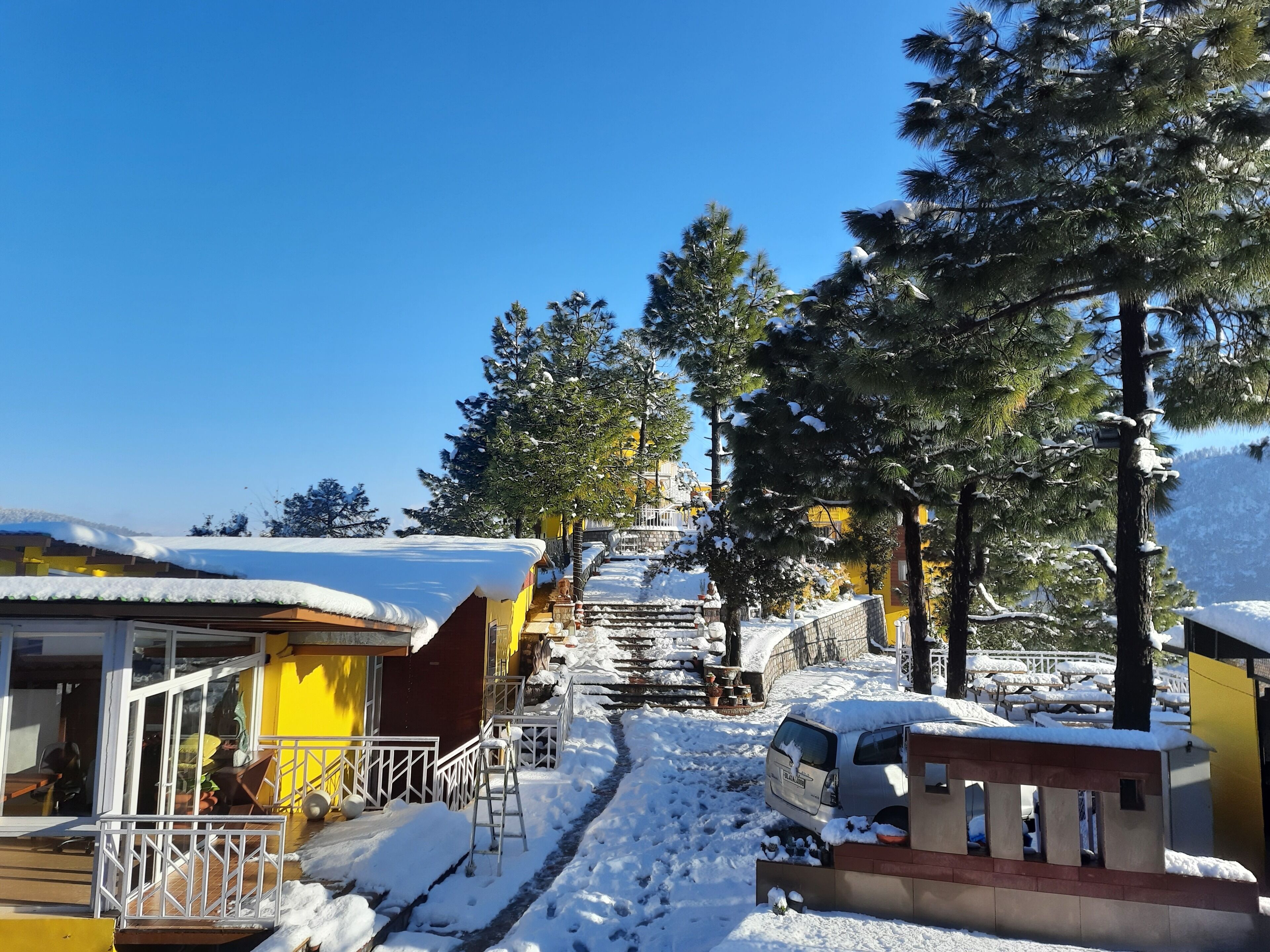 A snowy outdoor area with a yellow building, a covered walkway, and a car parked nearby.