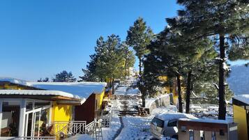 A snowy outdoor area with a yellow building, a covered walkway, and a car parked nearby.