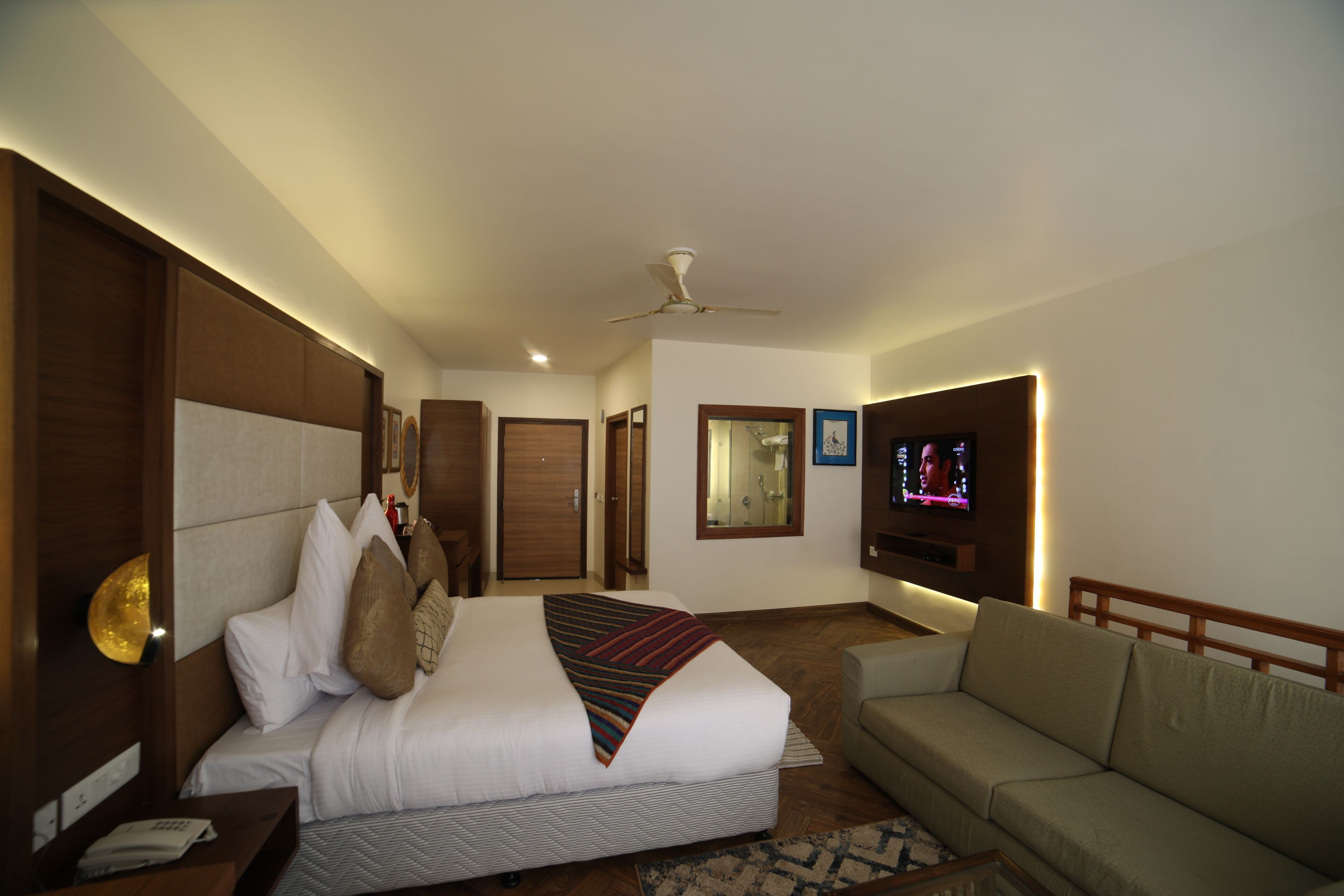 Una habitación de hotel con cama, sofá, televisor y ventilador de techo.