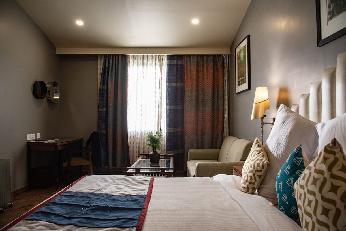 A hotel room with a bed, a desk, a chair, a lamp, and a window with curtains.