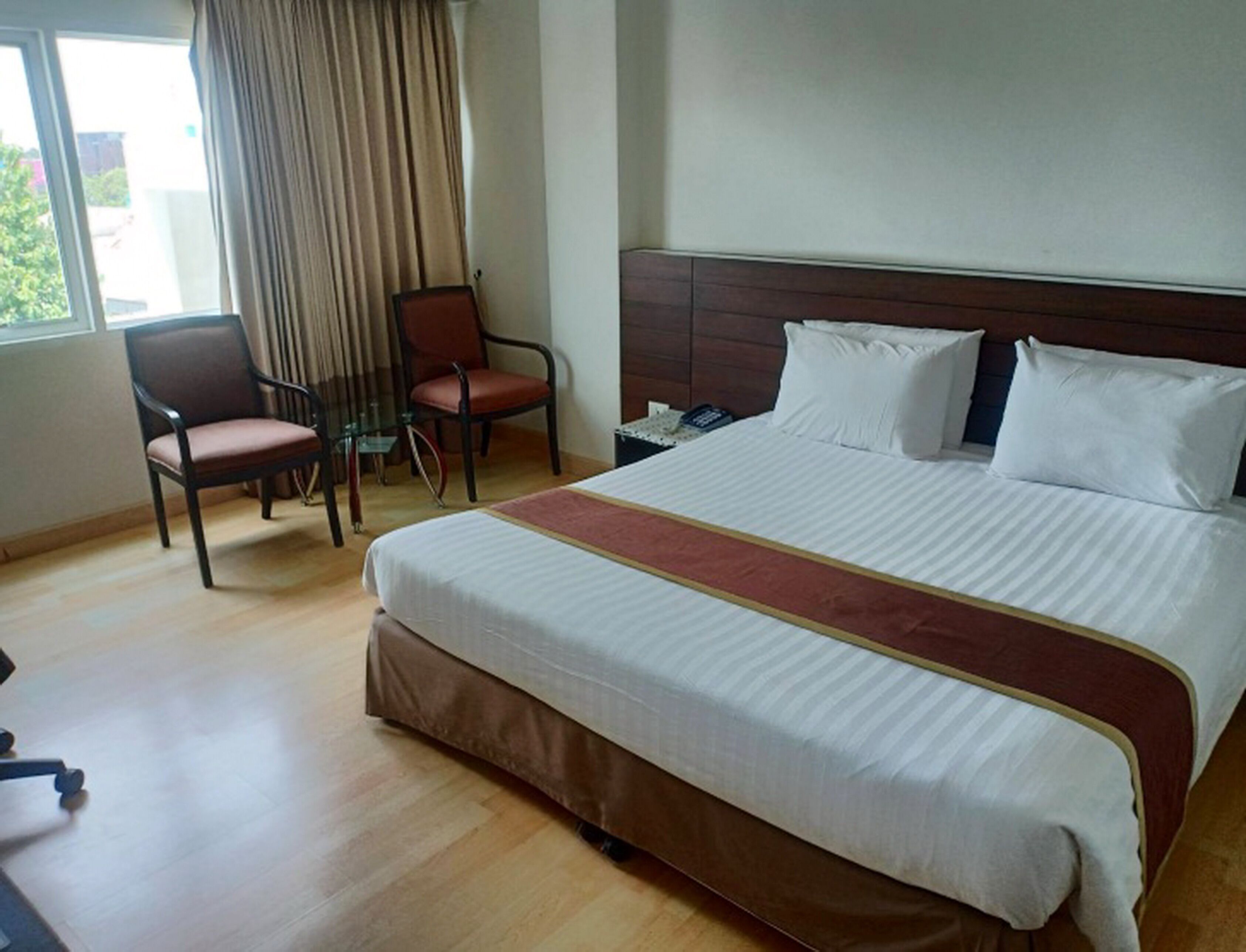 A hotel room with a large bed, a desk with a chair, and a window with curtains.