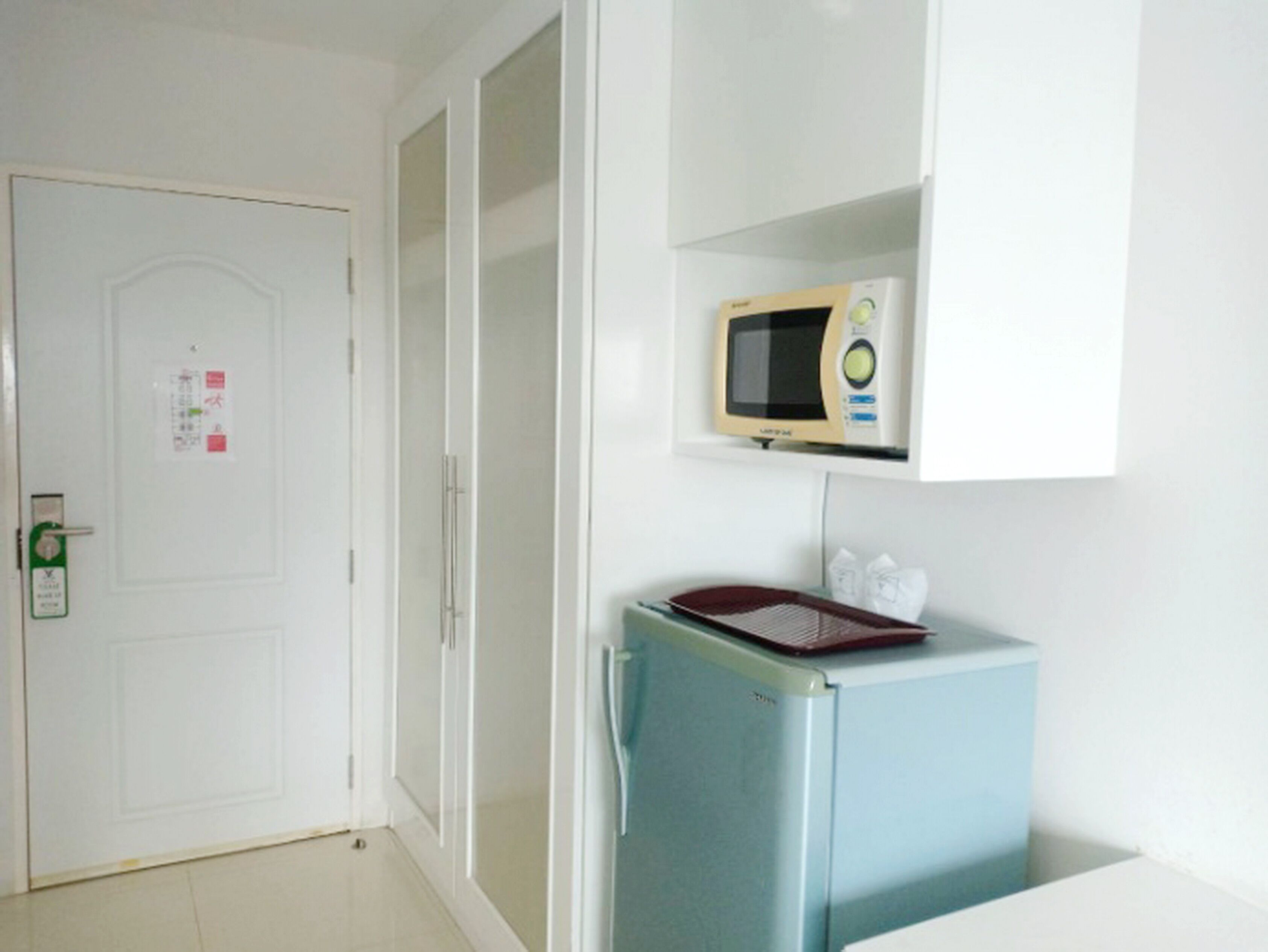 Una cocina pequeña equipada con microondas, refrigerador, una puerta con cerradura y un letrero.