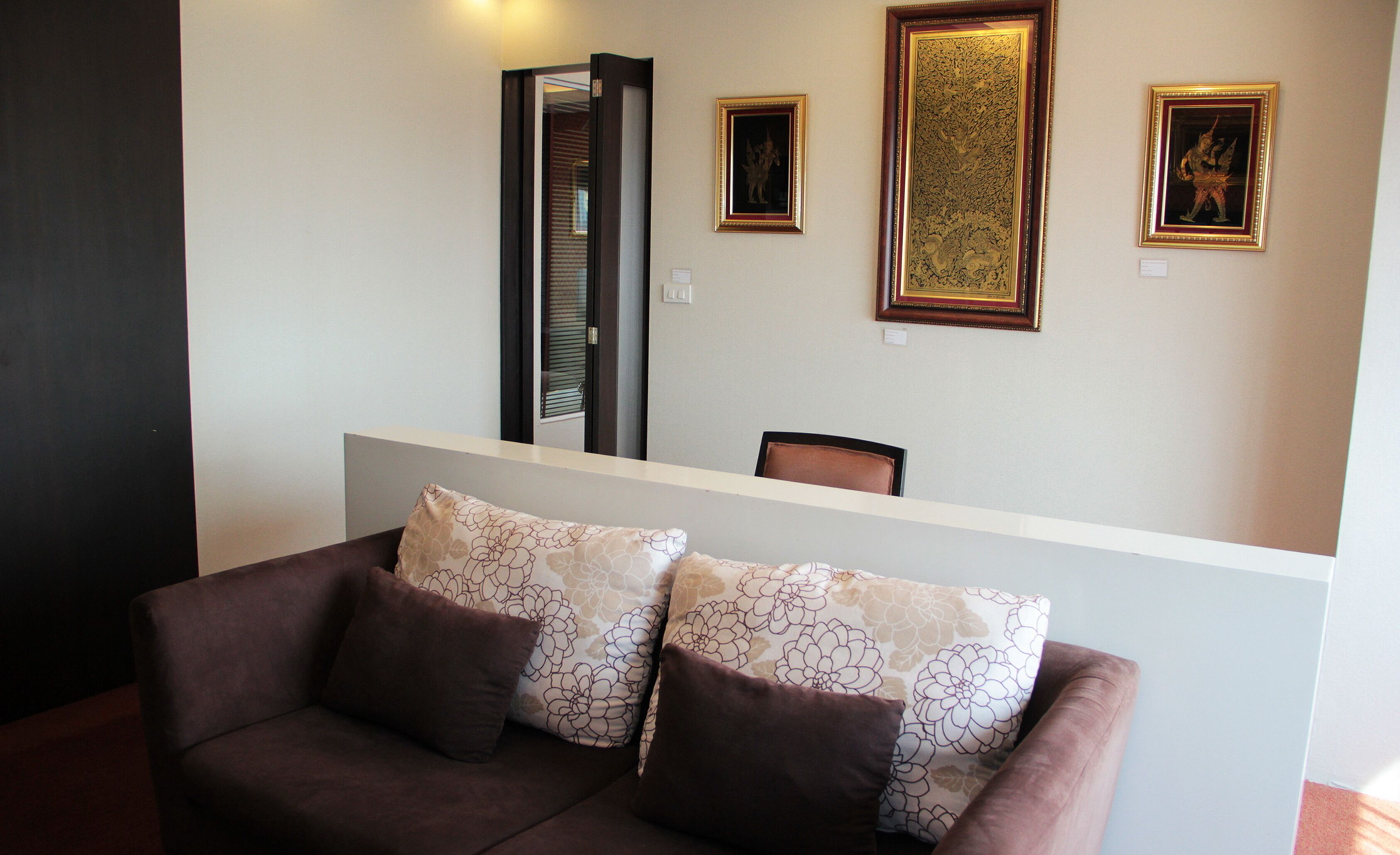 A reception area with a brown sofa, a wooden reception desk, and three framed artworks on the wall.