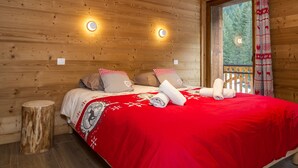 Ein Zimmer in einer Holzhütte mit einem Bett, zwei Wandleuchten und einem Fenster mit Vorhängen.